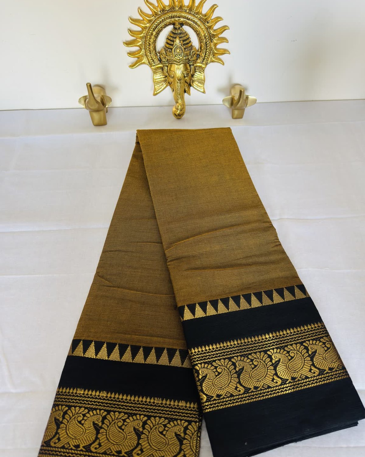 An olive-gold cotton saree with a black border of woven gold peacocks