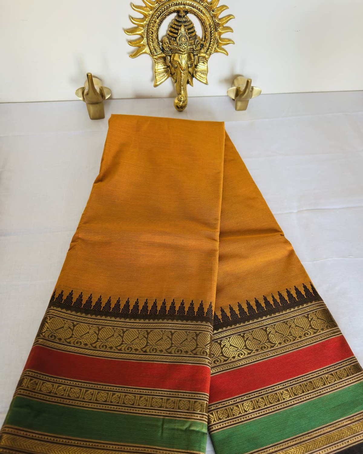 A yellow cotton saree with a border of gold peacocks and red and green stripes